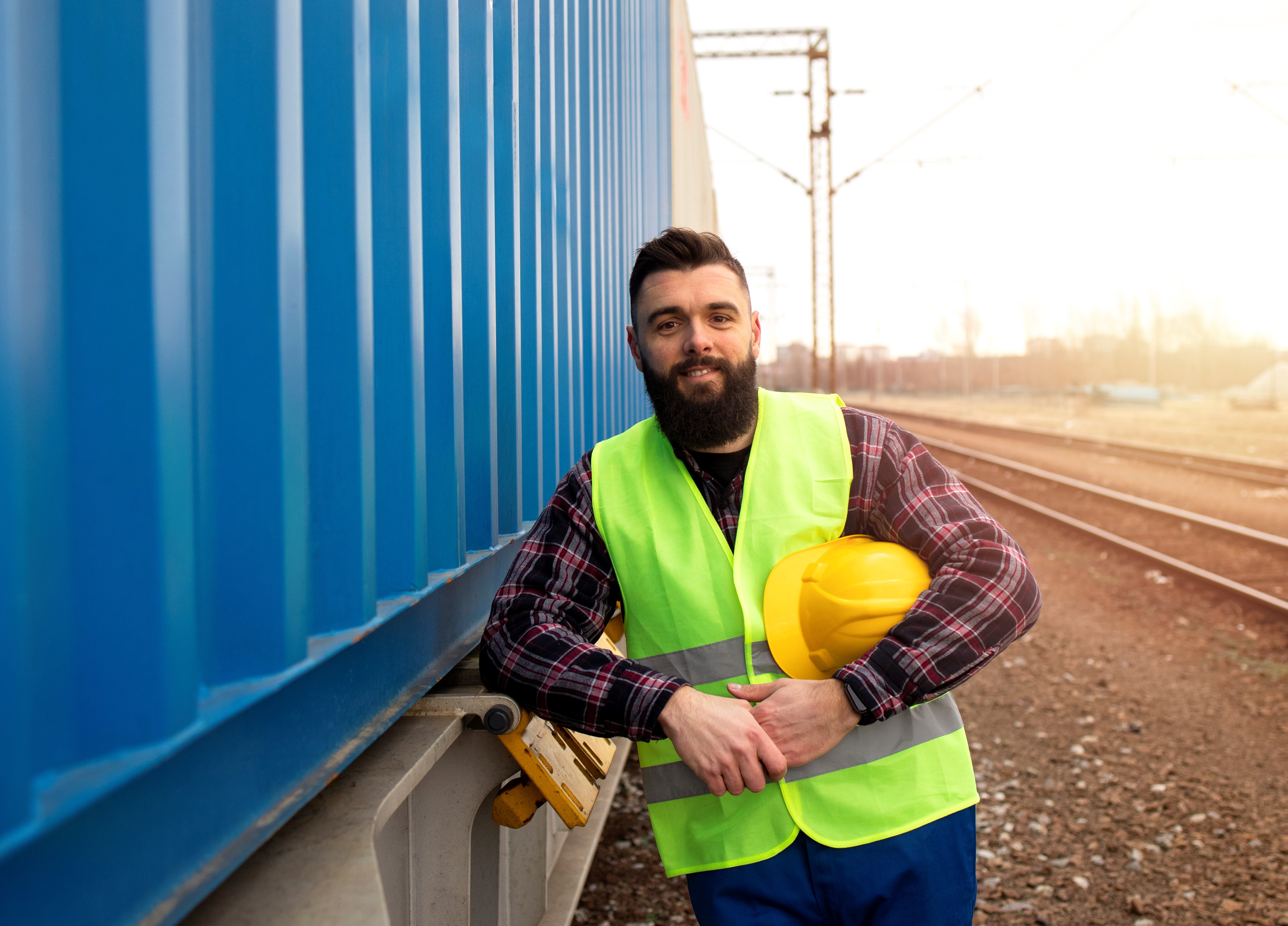 Man in high viz and holding hard hat by freight carriage