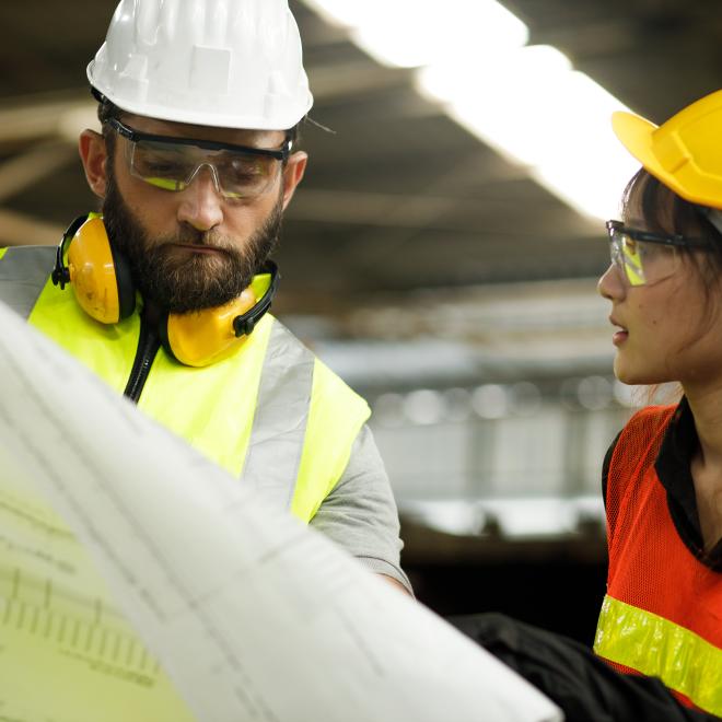 Man and young women in hard hats examining a chart.